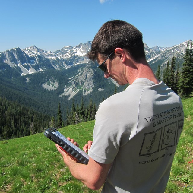Filed crew member recording data while standing on open slope with mountains in distance