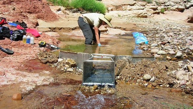 Person bends over in stream flowing through weir