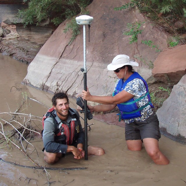 Two people in life jackets standing in river with monitoring equipment