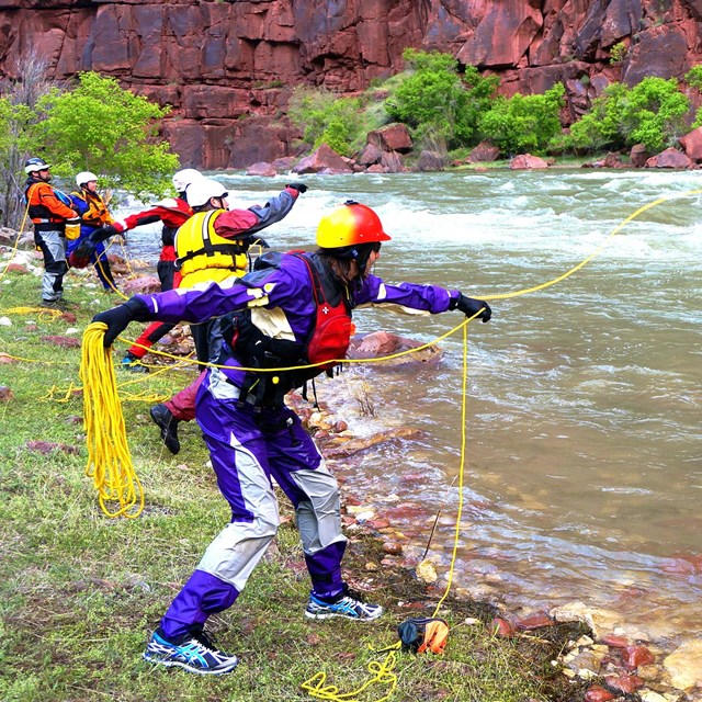 People in PFDs throw ropes from river bank