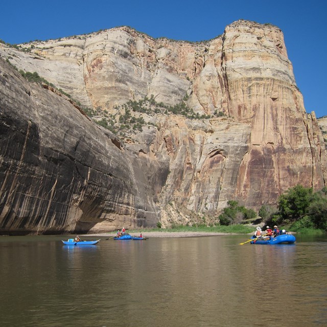 Four inflatable boats below a towering rock wall