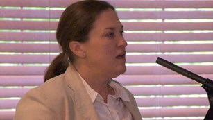 White female with hair pulled back in a ponytail wearing a cream-colored jacket over a white shirt.