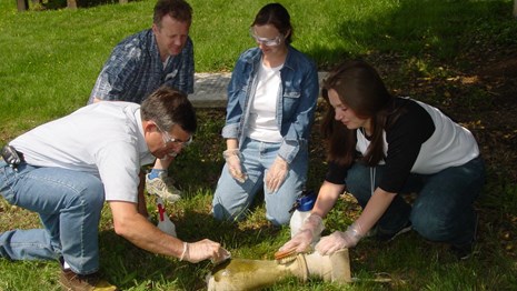 four people cleaning carving in cemetery
