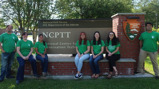 A group of interns stand in front of the NCPTT sign