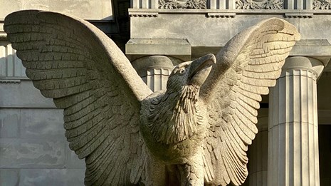 A grey granite statue of an eagle with its wings spread out in a v shape looking to the right