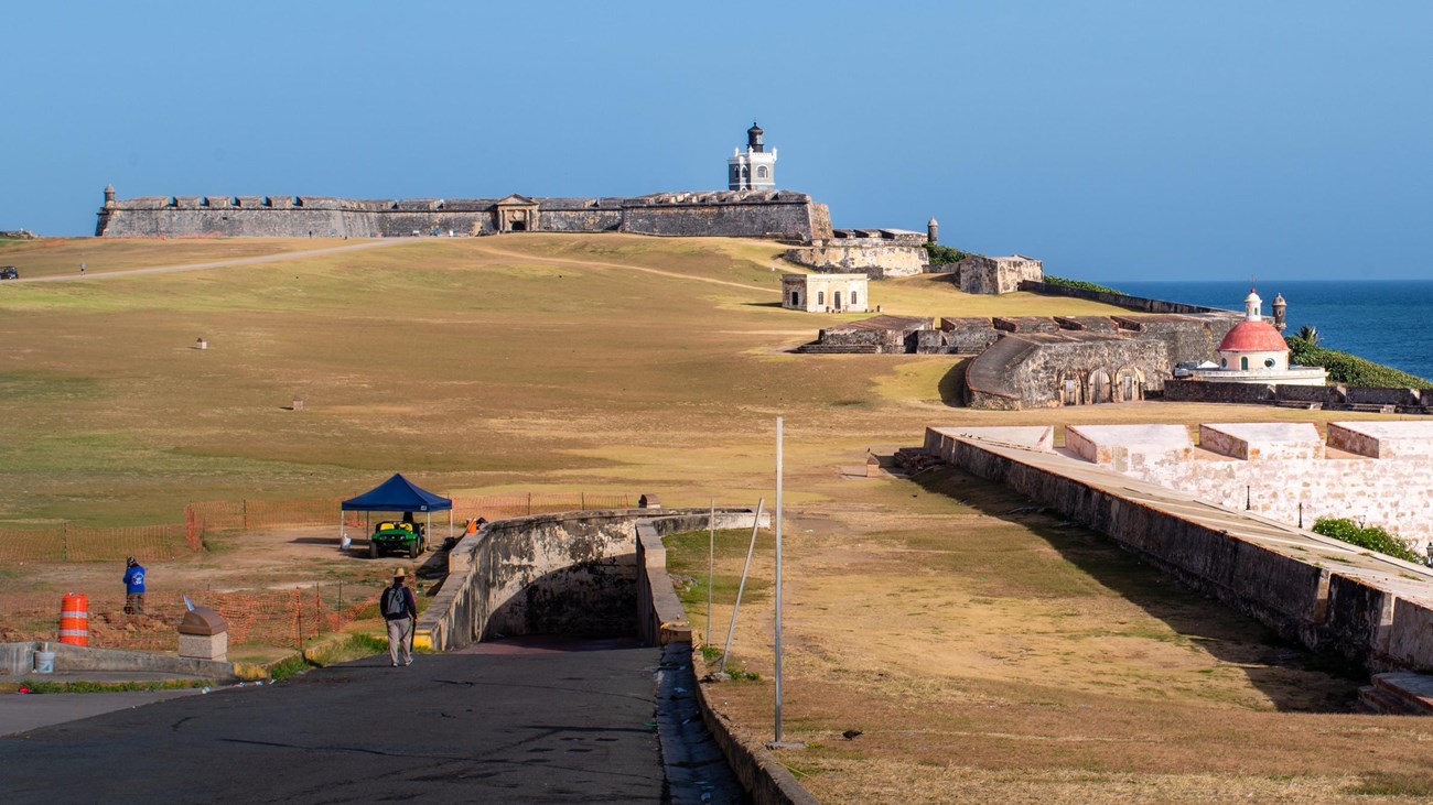 A large stone fort spans a green field with ocean behind