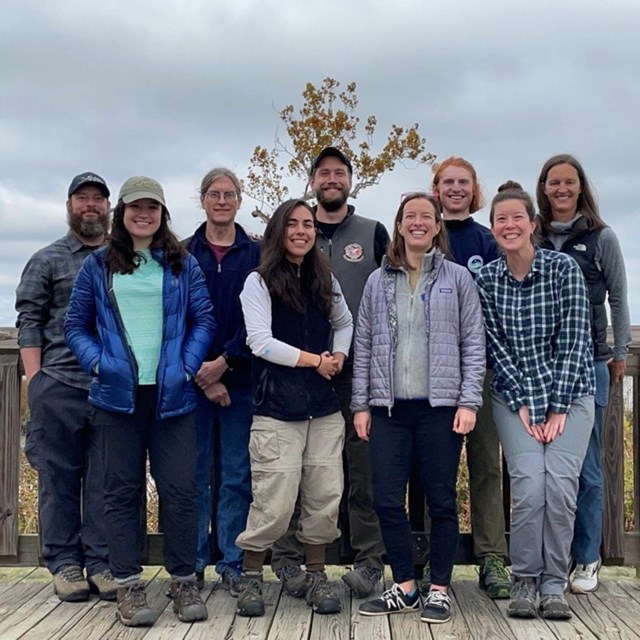 A group of ecologists poses on a boardwalk under an overcast sky