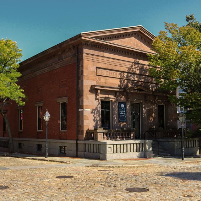 View of the stone visitor center building with green surrounding each side and a cobblestone road