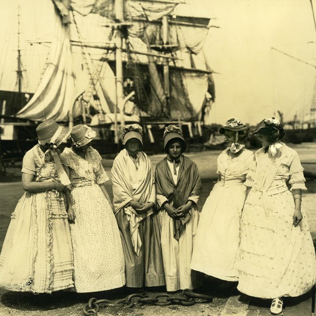 Six women stand on dock in front of ships in 1922.