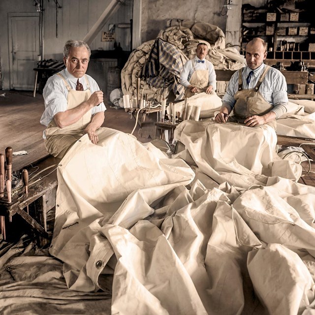 Historic colorized photo of sail loft workers sewing sails.