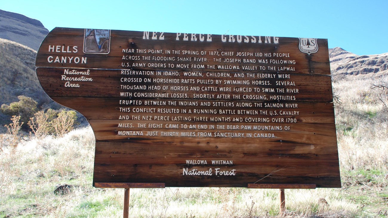 A wooden sign about the Nez Perce Crossing at Dug Bar with canyon walls in the background.