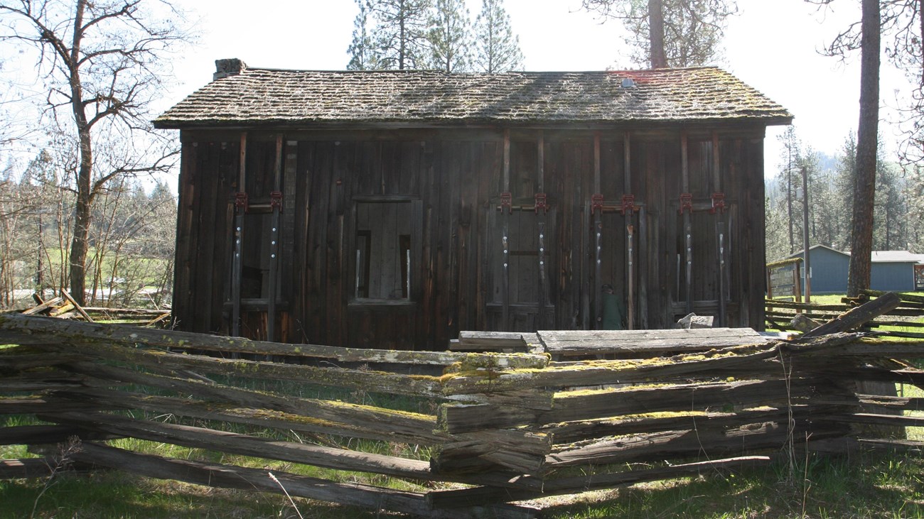 A dark brown two story wood house with a wood fence in front.