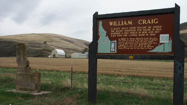 A dark brown sign with the words 'William Craig' on it next to a monument in the shape of Idaho.