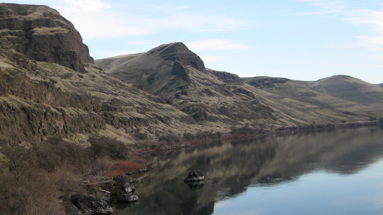 A steep rocky mountain side along a river.