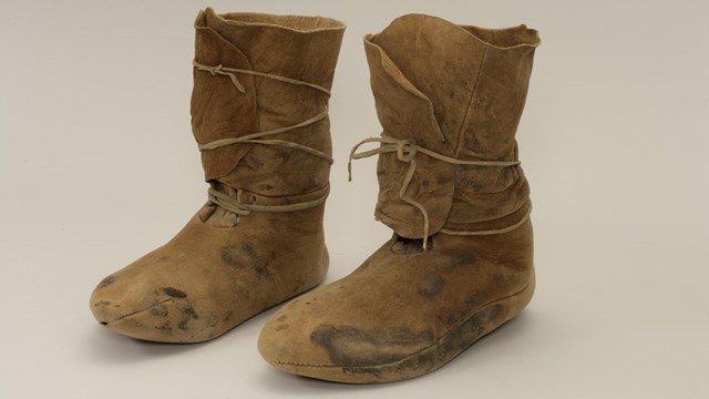 A pair of tall, tan buckskin moccasins sits on a white background.