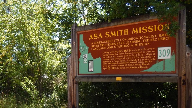 A dark brown sign with a trees in the background on a sunny day.