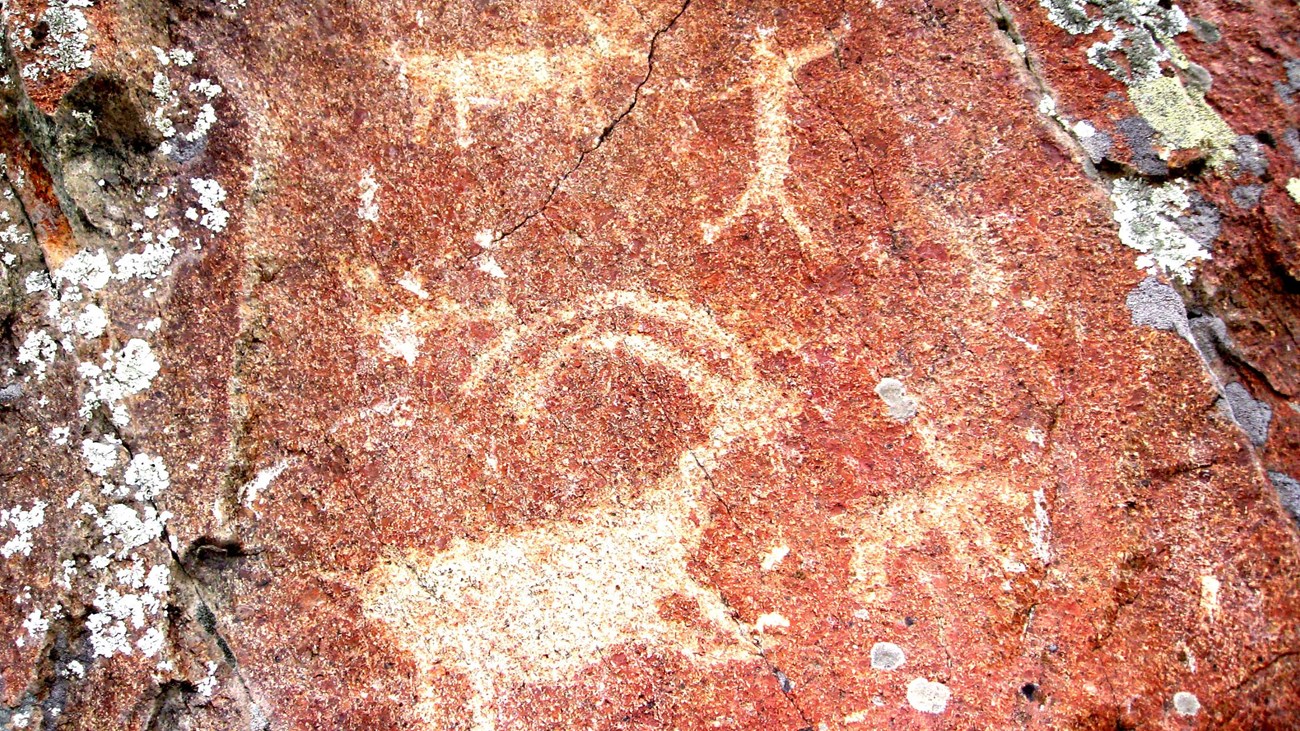 A red rock with several white petroglyphs on the rock surface.