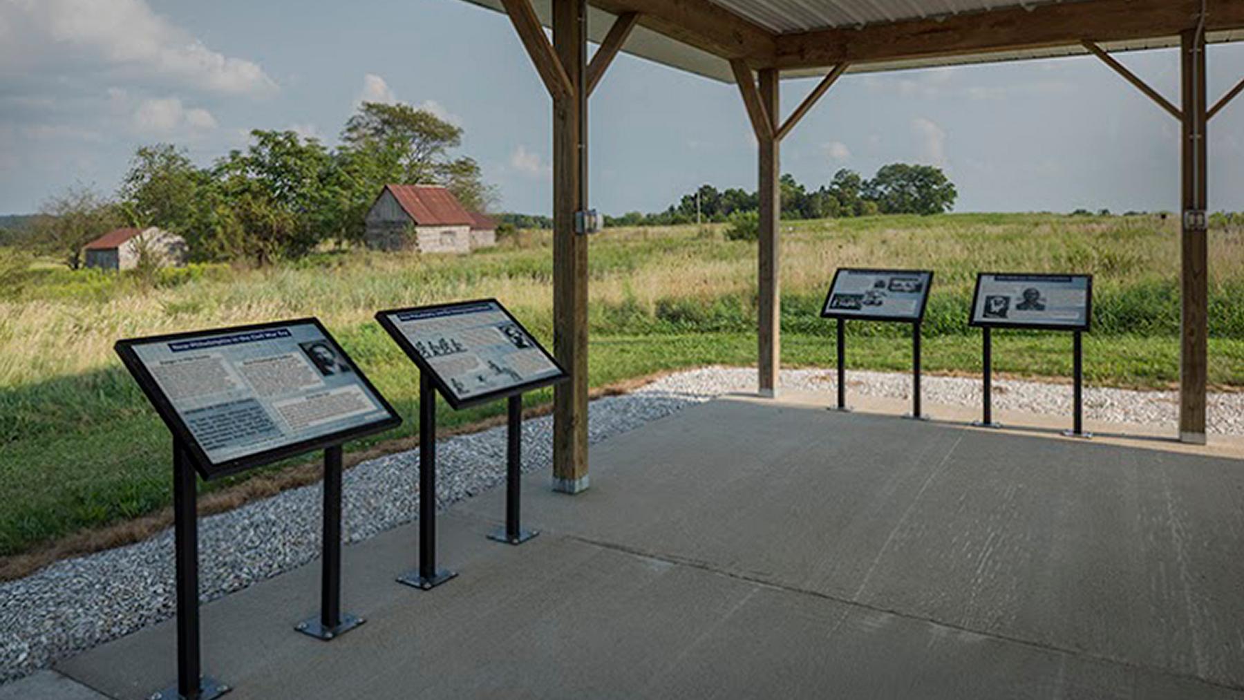  Four interpretive panels mounted under a covered, kiosk overlooking a prairie landscape.