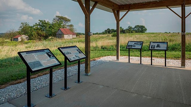  Four interpretive panels mounted under a covered, kiosk overlooking a prairie landscape.