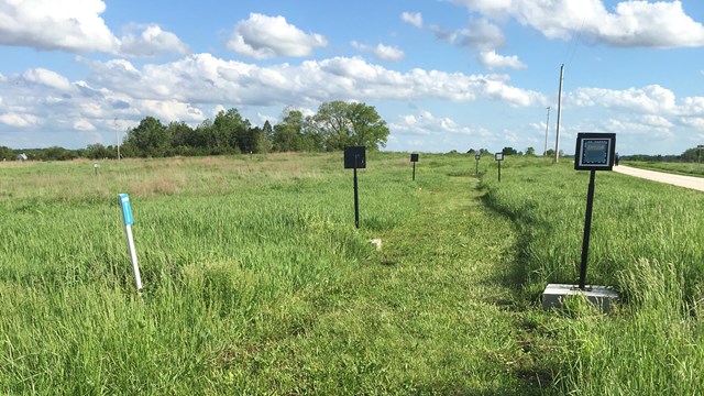 A mowed path through prairie. There are numbered signs along the trail for a tour. 