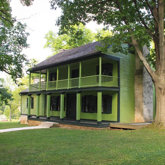 A bright green two-story frame house with open first and second floor porches.