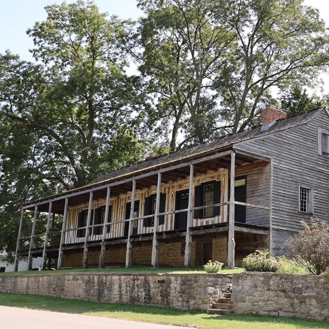 Raised home with a covered porch. Vertical log construction and a stone foundation are visible.