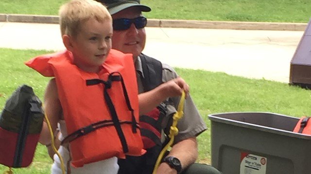 Young boy with life jacket practices using a throw rope