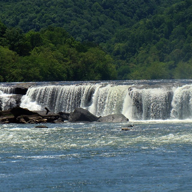 A wide river cascading 10 to 20 feet over rocks forming a wide waterfall.