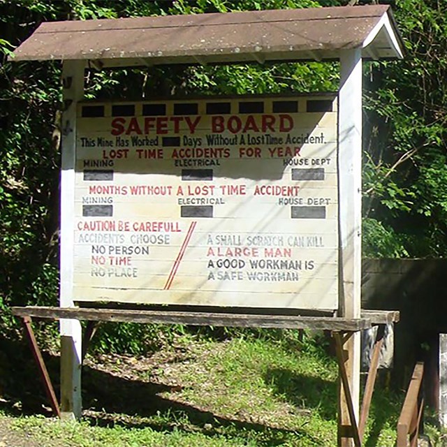 A large wooden sign that says Safety Board in front of a ruined stone building