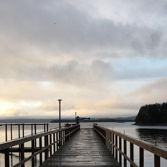 Looking out over a wooden pier at small islets and mountains on the water's horizon