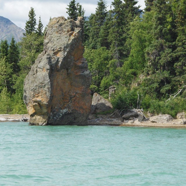 A view over the water of Lake Clark of Priest Rock and vibrant forests in the background.