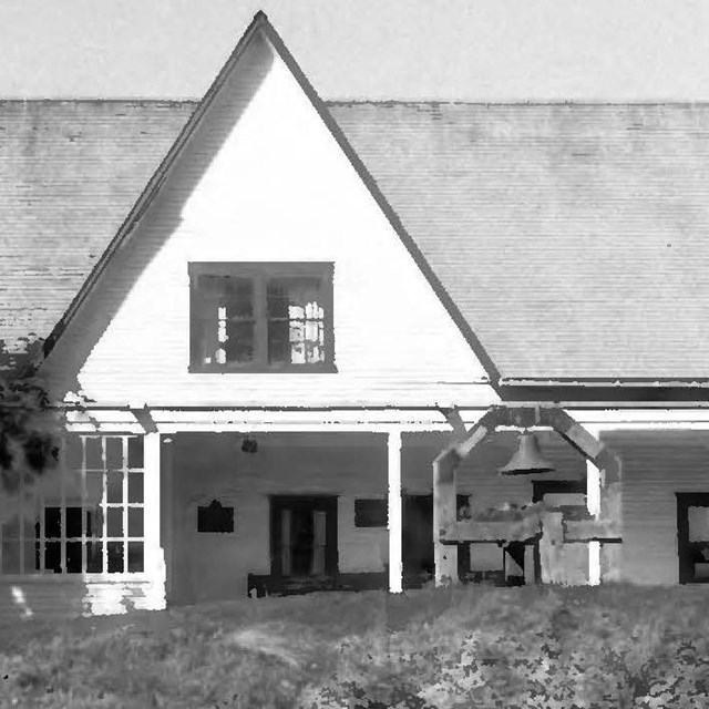 Black and white photo of the Russian-American Co. Magazin with white walls and a steep gray roof wit