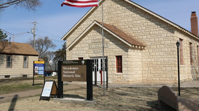 corner view of a large limestone building with white doors with glass panels and a brown lawn