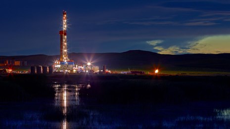 An oil rig drilling site emits bright lights into the atmosphere.