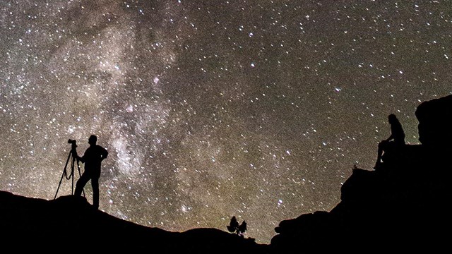 Silhouetted view of people stargazing against a vast backdrop of night sky