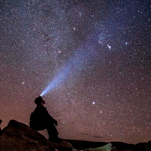 a silhouette of a person with a head lamp in front of a starry night sky