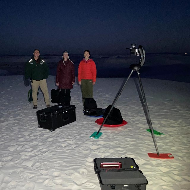 three researchers stand next to equipment for measuring night sky brightness