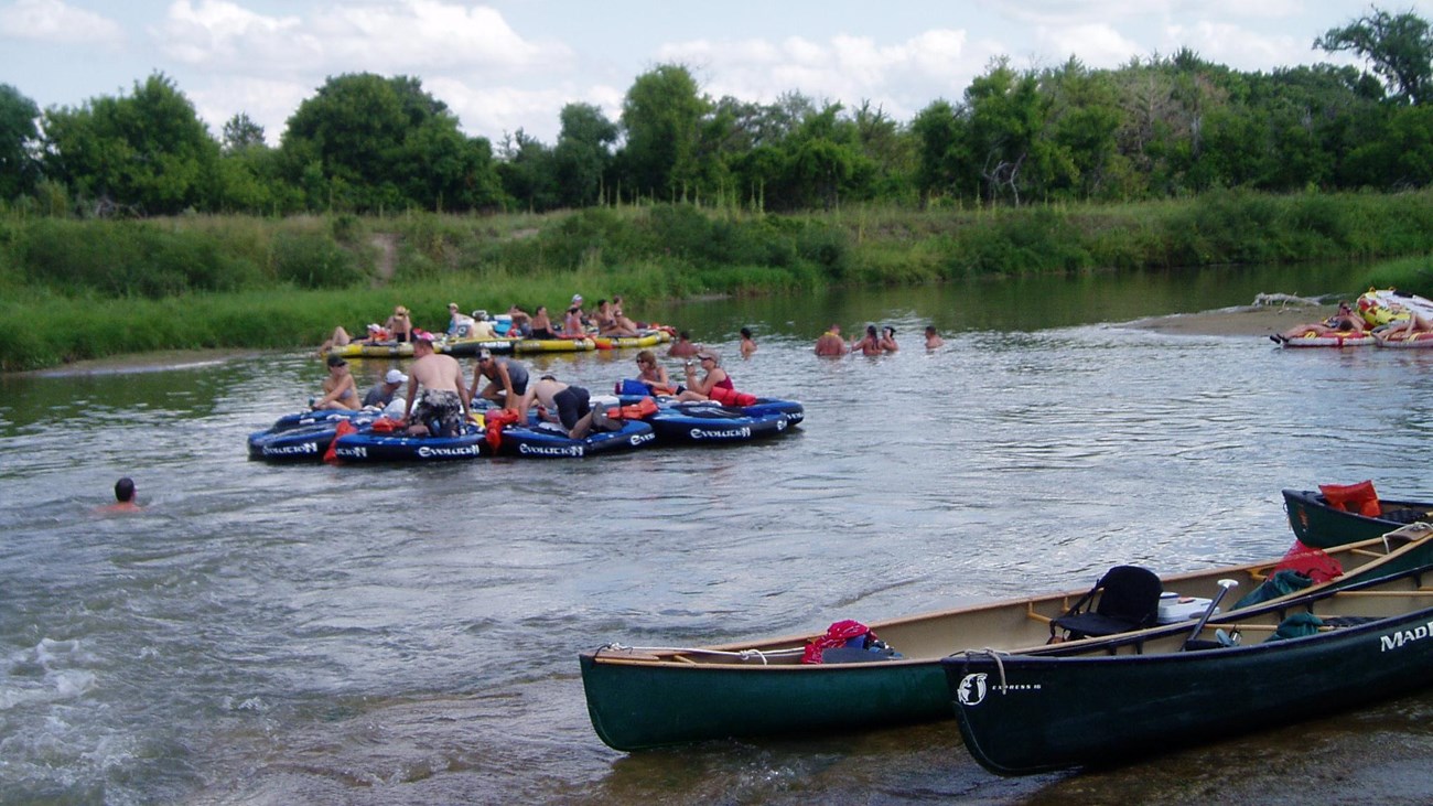 A group of tubes on a river with two canoes on the sandy shore.