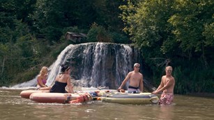 In a still shot from a video, four people float on tubes in front of a waterfall on the Niobrara.