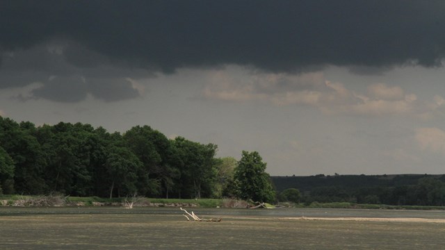 A storm with dark clouds brews over a calm river.