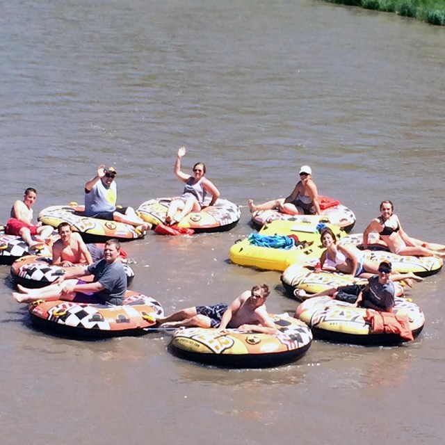Tubers in a circle on the river waving to the camera