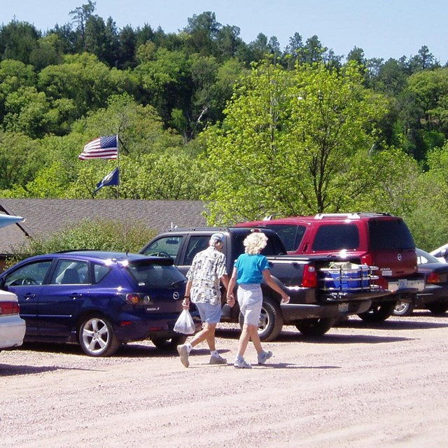 Visitors and cars in a gravel parking lot on a sunny day