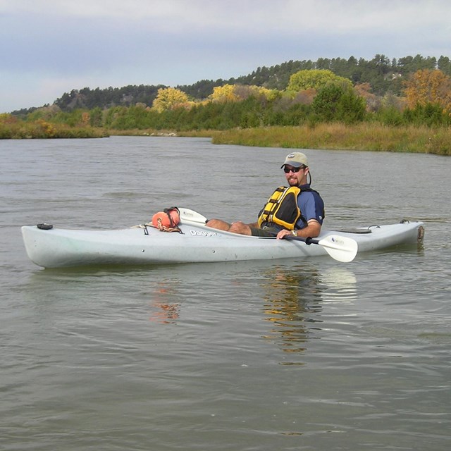 Kayaker in grey vessel on calm water.