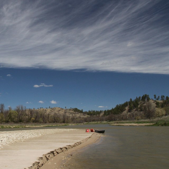 A sandbar extends into a calm river in summer with clouds above
