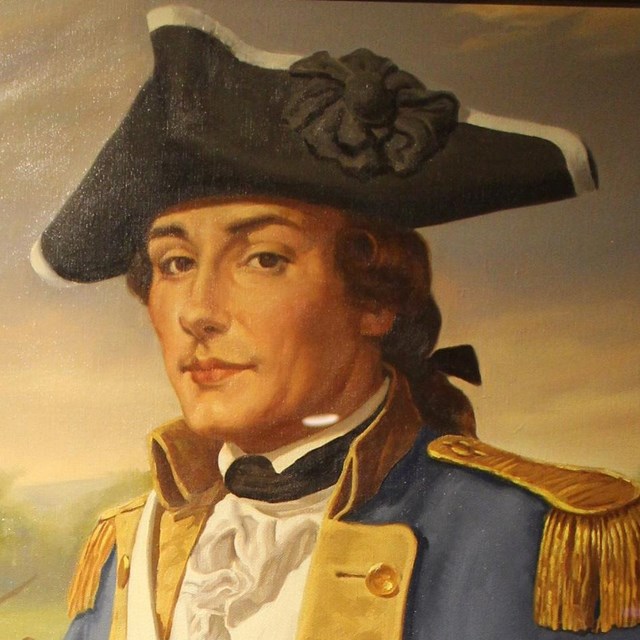 A man in a black hat and light blue coat pointing at a map on a table. 