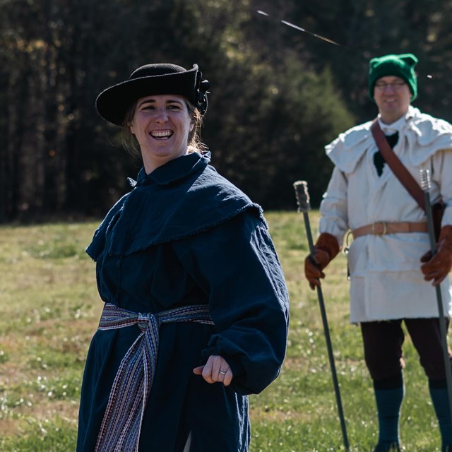 A woman dressed in a man's navy blue hunting frock and white breeches. 