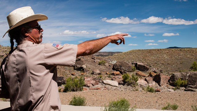 man in a cowboy hat points right while standing in a rocky terrain