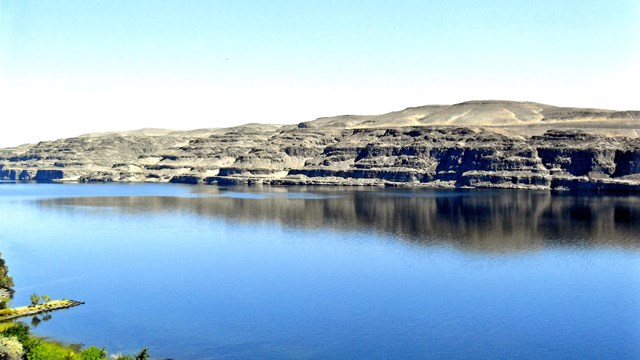 a calm body of water with a dry hilly landscape beyond