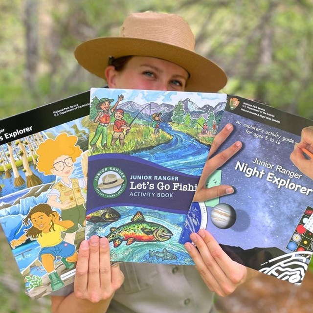 a park ranger holds up three junior ranger books