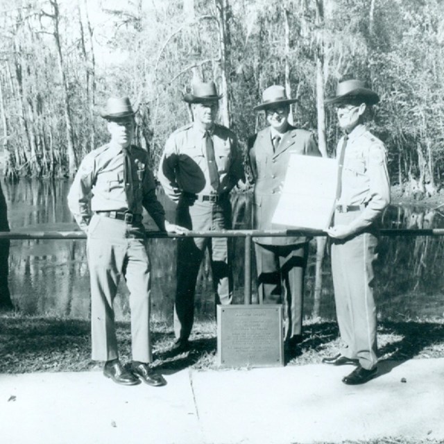 people standing next to plaque with pond in background